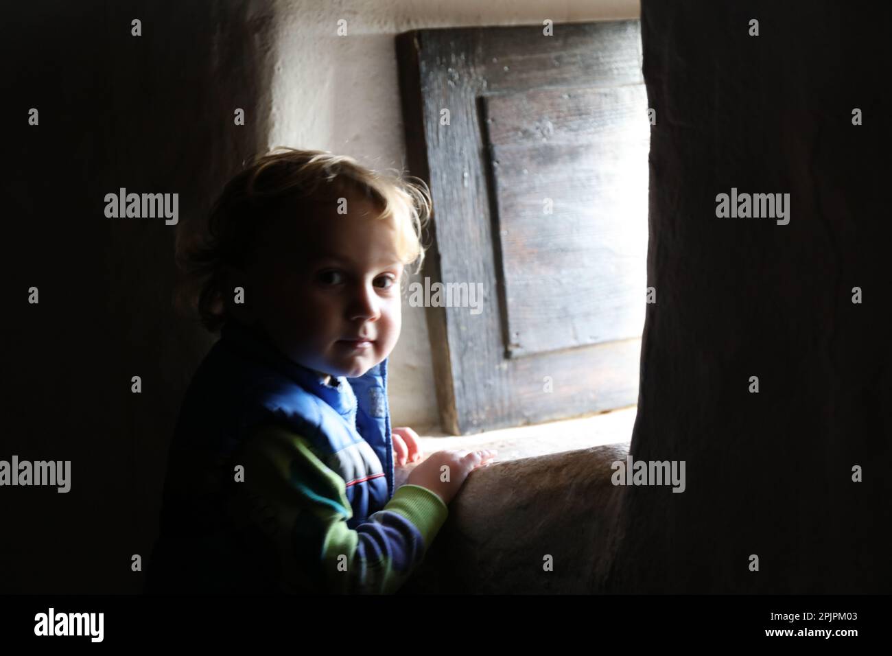 Ein blonder, kaukasischer kleiner Junge, der aus einem alten Fenster schaut Stockfoto