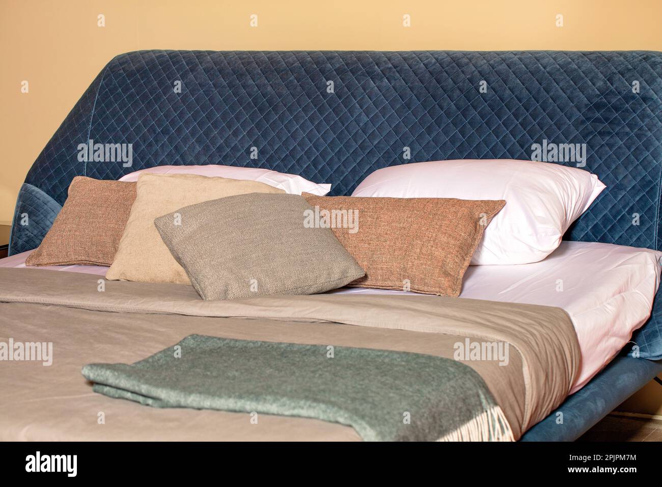 Ein Teil des Schlafzimmers mit ausklappbarem Sofa, gestepptem blauem Kopfteil aus Velor und weichen Kissen. Stockfoto