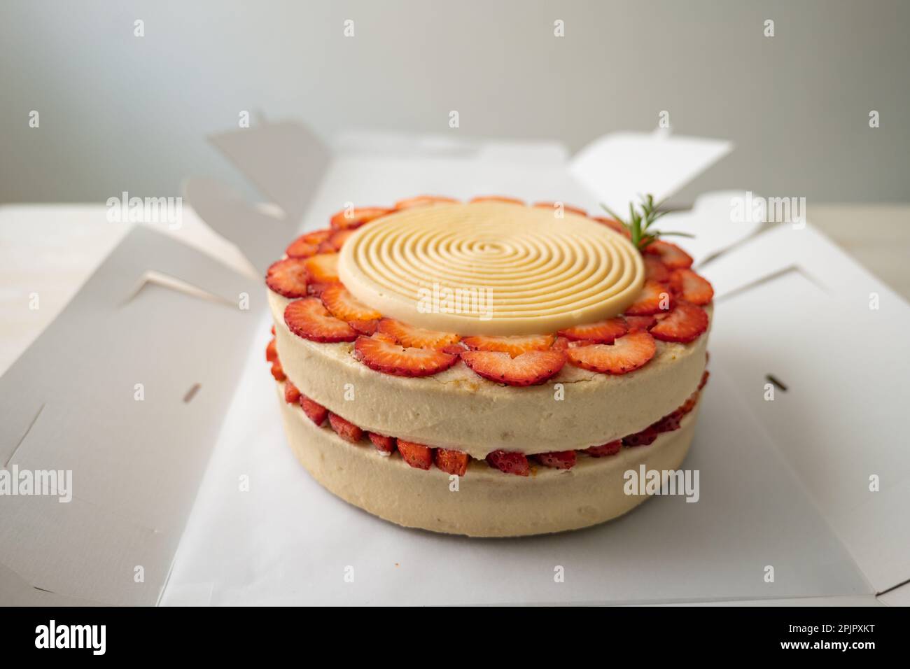 Veganer Geburtstagskuchen mit Vanille und Erdbeere, bedeckt mit weißer Schokolade in einer geöffneten Pappschachtel auf einem Tisch und weißem Hintergrund Stockfoto