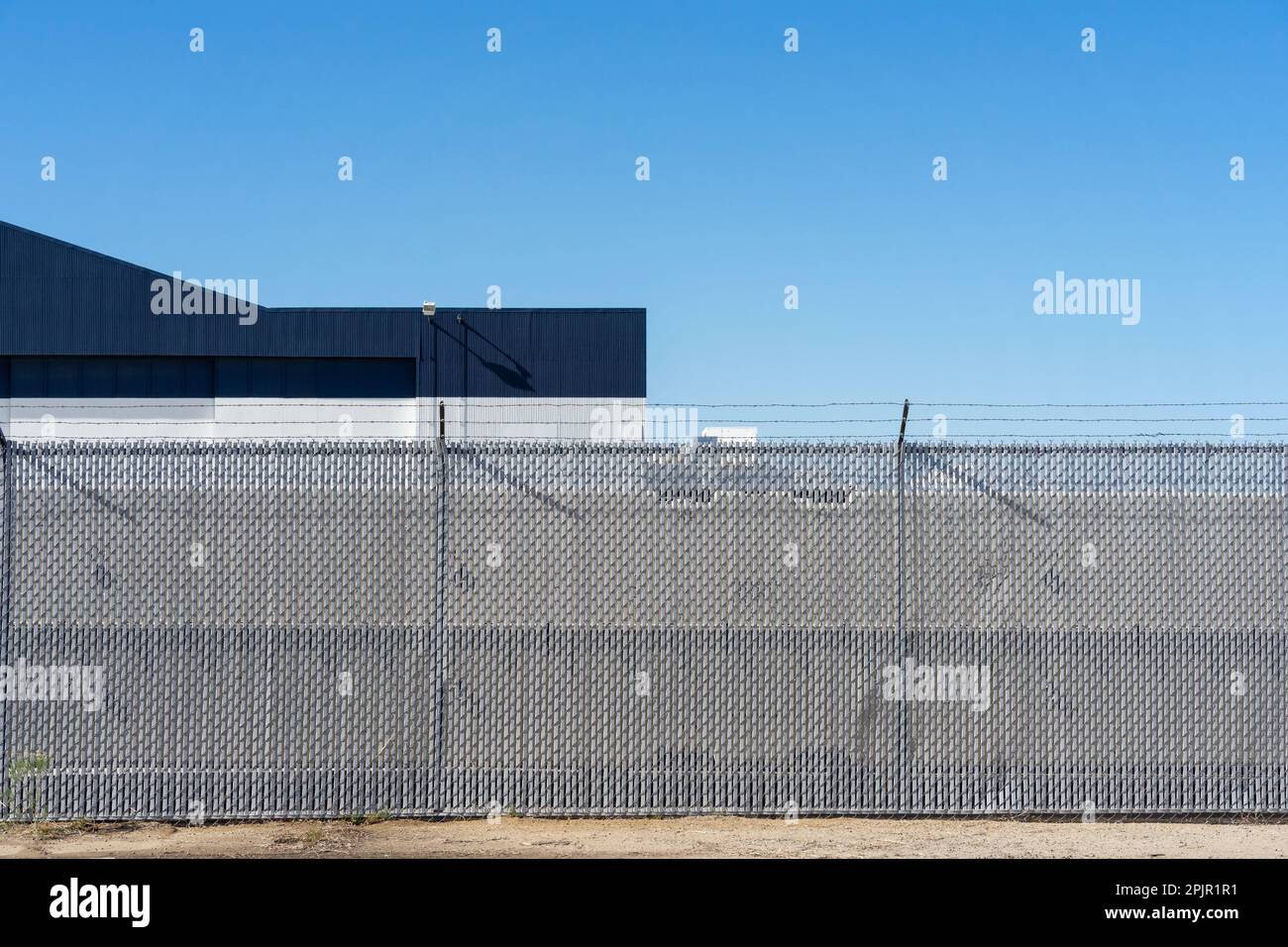 Sicherheitszäune mit Kettengliedern mit Vinylleisten und Stacheldraht-Topper vor einem Gebäude Stockfoto