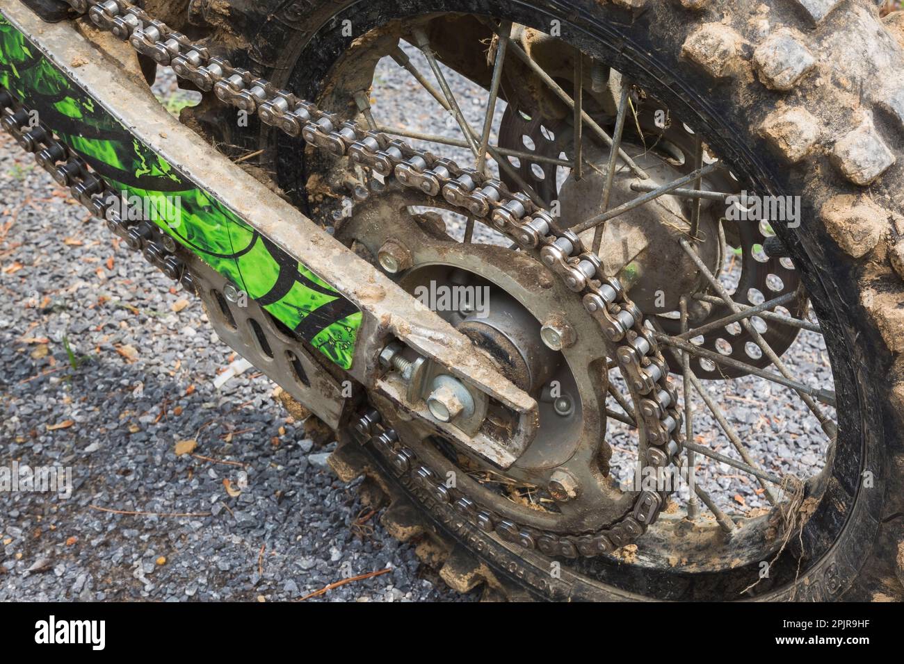 Kette und schwarzer hinterer Gummireifen, der mit getrocknetem Schlamm auf einem auf Schotterstraßen geparkten Motorrad bedeckt ist. Stockfoto
