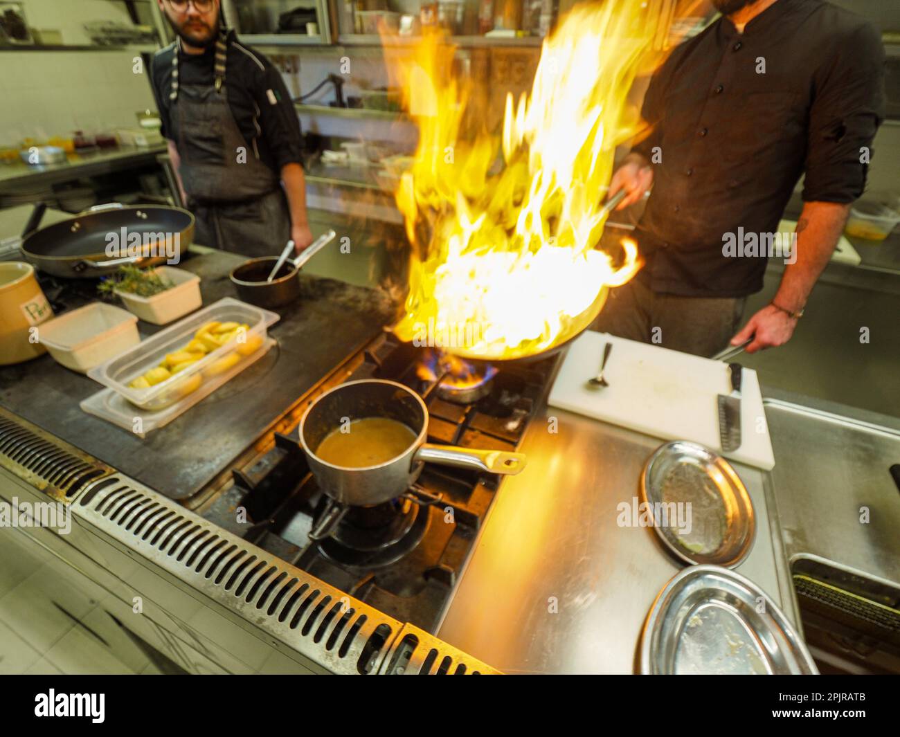 Koch kocht flamblendenden atlantischen Tintenfisch mit Olivenöl in einer großen Pfanne in einer professionellen Küche, trendige Meeresfrüchte-Rezepte, professionelle Gourmetküche Stockfoto