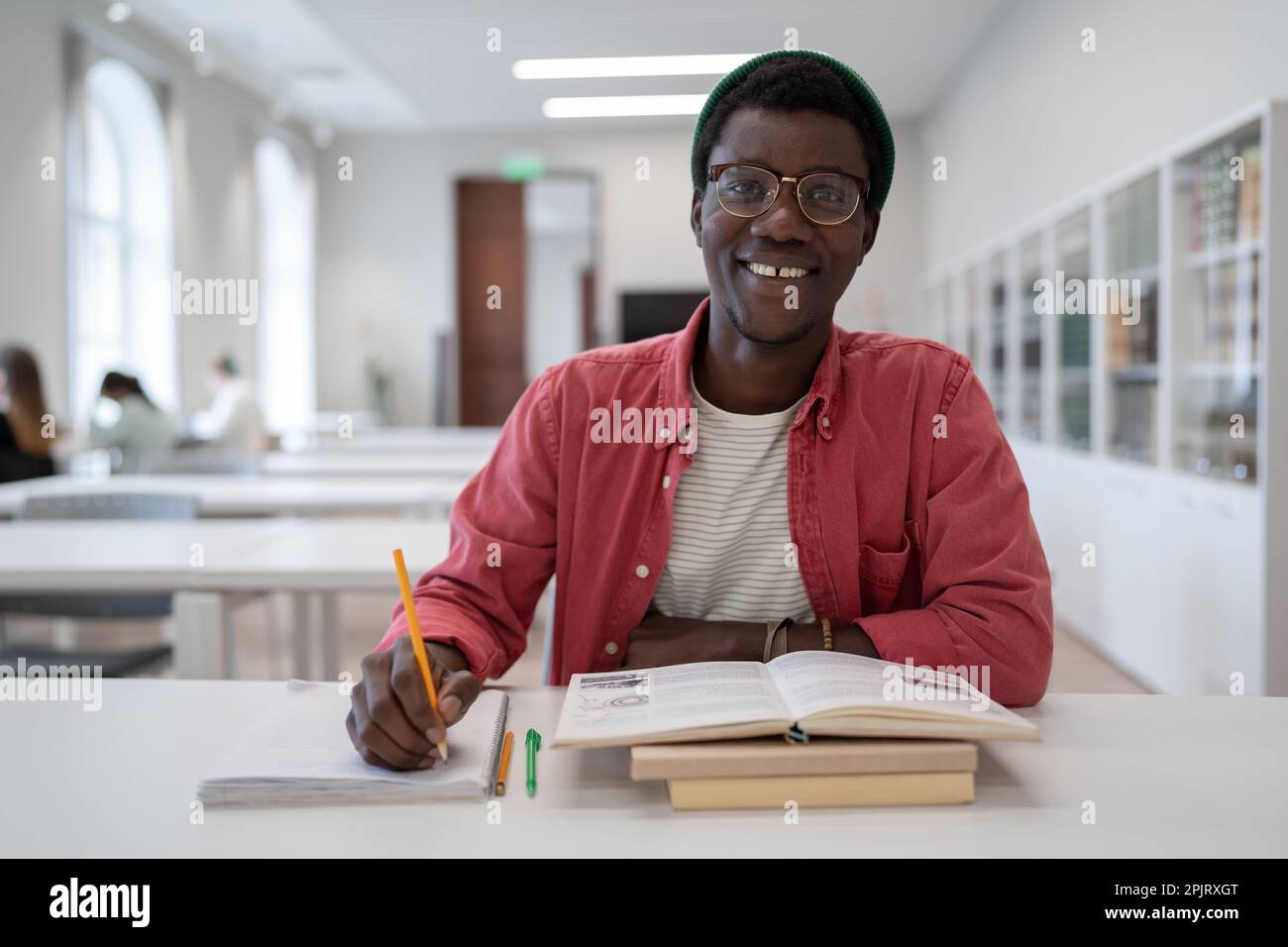 afroamerikanischer junger Mann, der in einer Universitätsbibliothek studiert und Notizen in Notizblock macht. Stockfoto