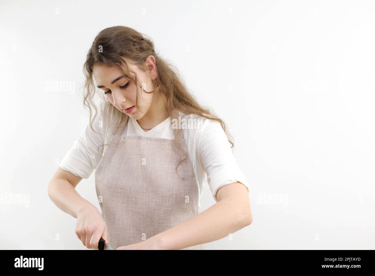 Ein junges Mädchen, das sich umgebogen hat, schneidet etwas aus der Nähe, das Gesicht eines angelehnten Mannes in einer Schürze. Der Koch bereitet in der Küche zu kochen. Ein weißes T-Shirt auf einer weißen Hintergrundwerbung Stockfoto