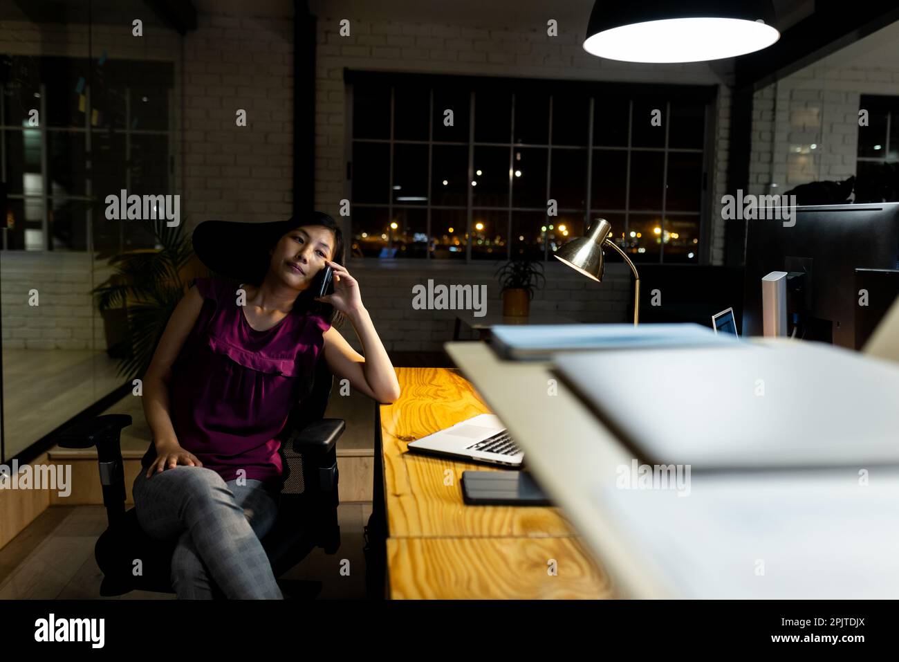 Asiatische Geschäftsfrau sitzt am Schreibtisch, telefoniert über ein Smartphone, arbeitet bis spät in die Nacht im Büro Stockfoto