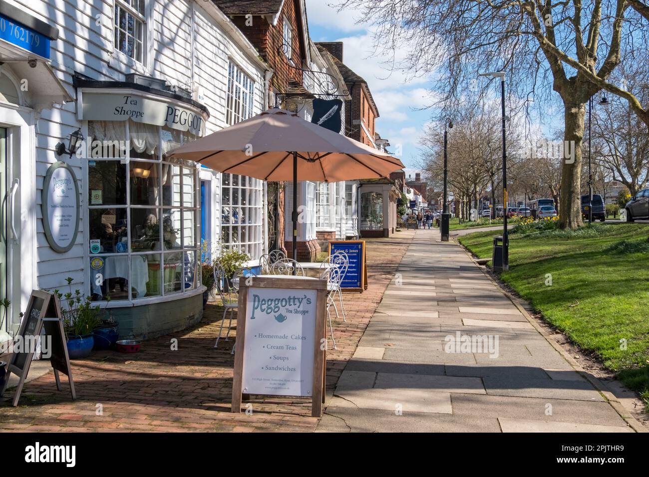 Geschäfte und Cafés auf dem breiten Bürgersteig in der Tenterden High Street, Kent, Großbritannien Stockfoto