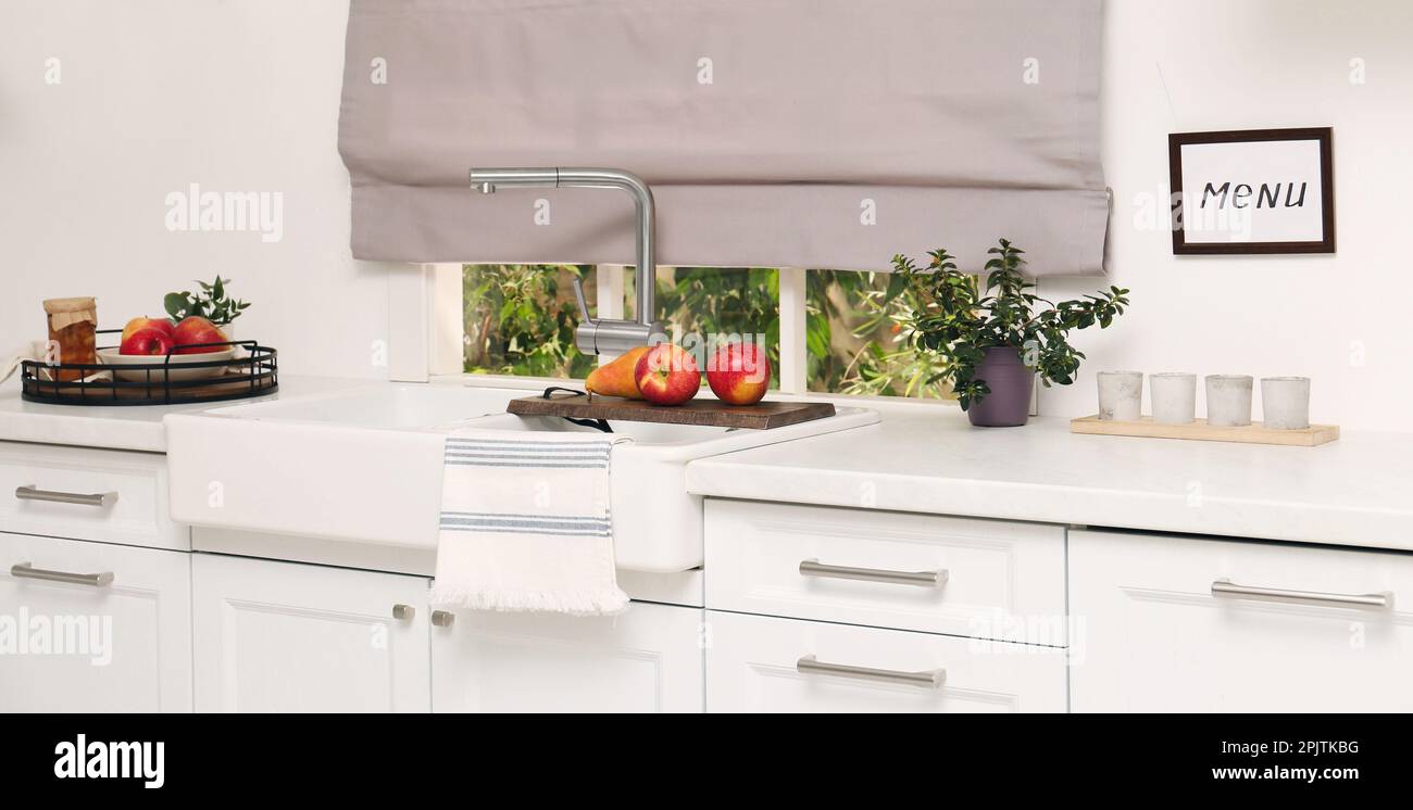 Weiße Küche mit Doppelwaschbecken vor dem Fenster und frischem Obst Stockfoto