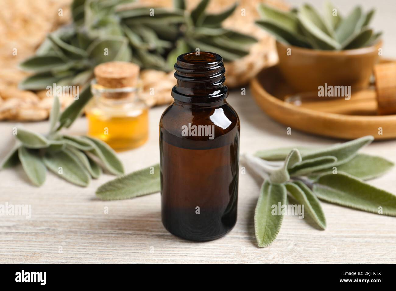 Flasche ätherisches Salbeiöl und Blätter auf Holztisch Stockfoto