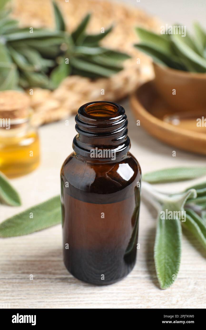 Flasche ätherisches Salbeiöl und Blätter auf Holztisch Stockfoto