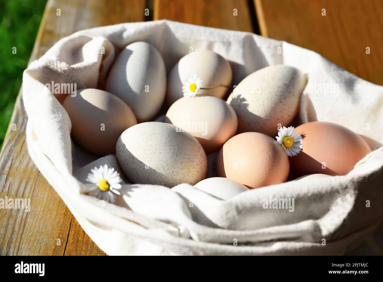 Sack mit verschiedenen Eiern und Kamillenblumen auf einem Holztisch im Freien, Nahaufnahme Stockfoto