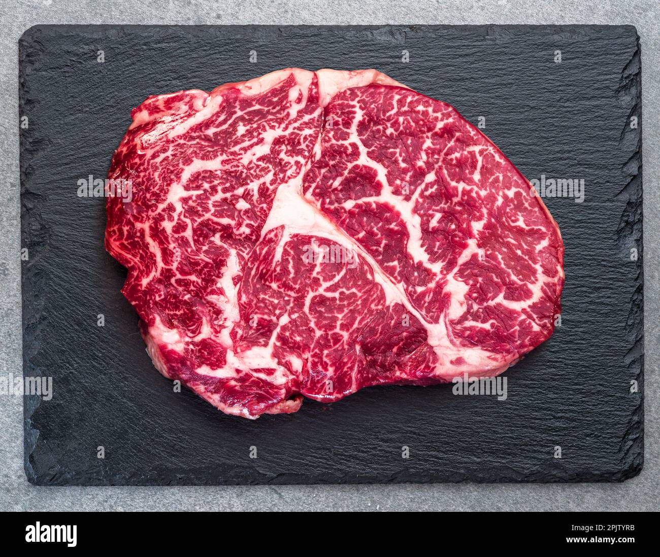 Rohes Ribeye Steak auf steinschwarzem Servierteller. Flach verlegt. Stockfoto