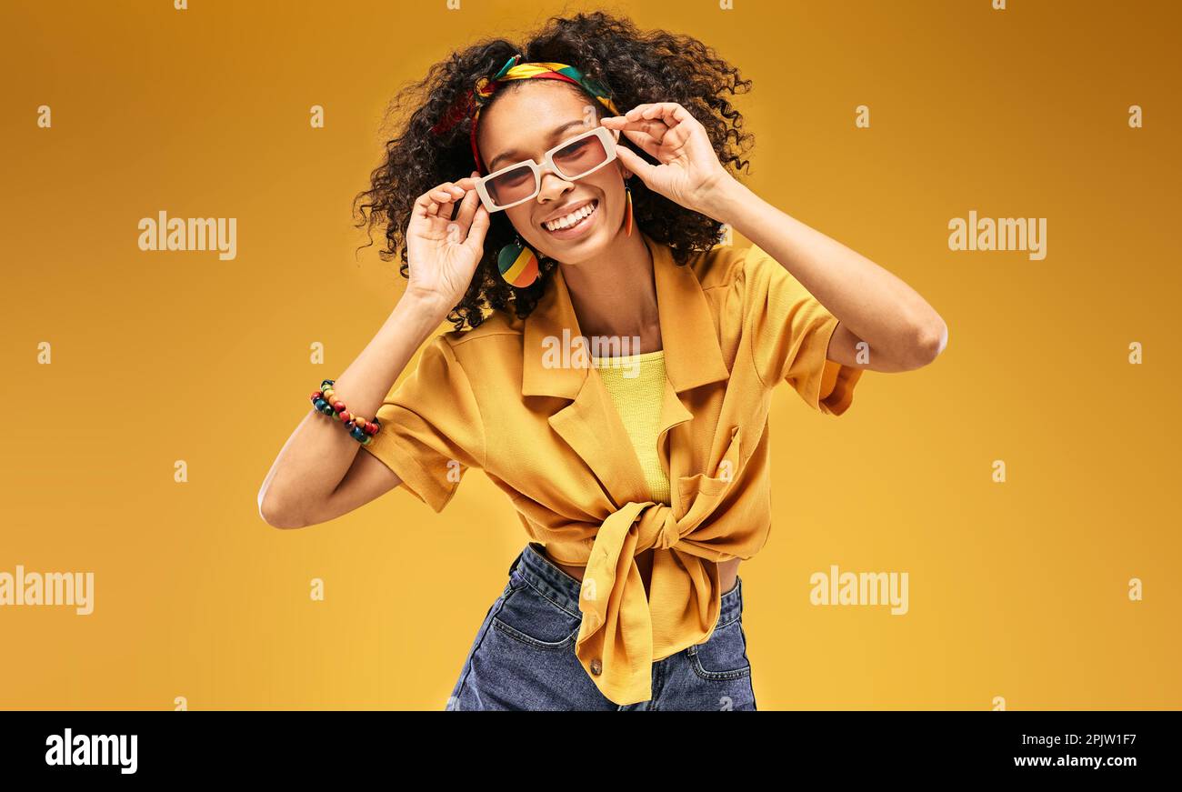 Glückliche afroamerikanische Frau in trendigen weißen Sonnenbrillen und gelber Kleidung auf gelbem Hintergrund, die fröhlich lacht Stockfoto