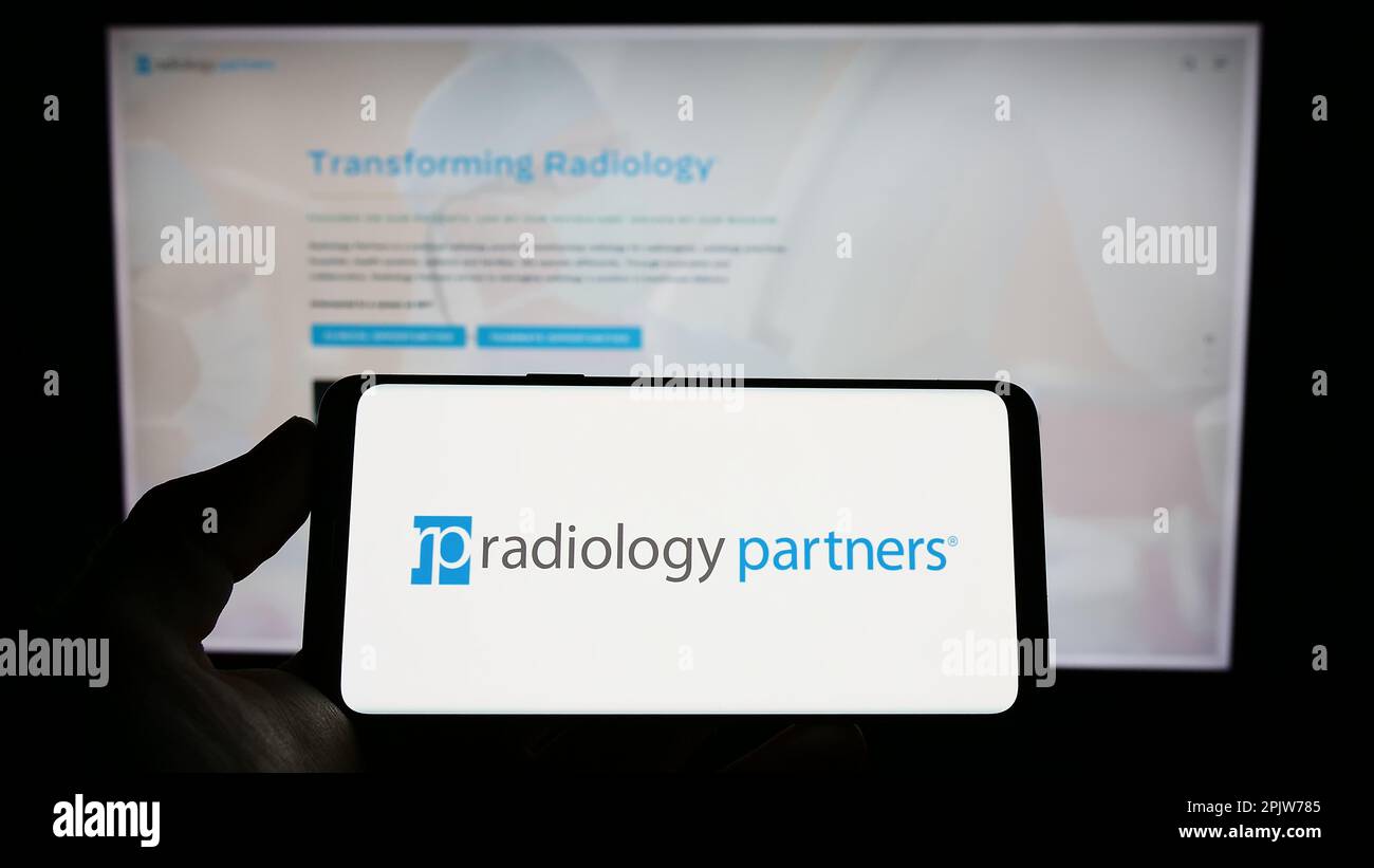 Person, die ein Mobiltelefon mit dem Logo des US-Gesundheitsunternehmens Radiology Partners Inc. Auf dem Bildschirm vor der Business-Webseite hält. Konzentrieren Sie sich auf das Display des Telefons. Stockfoto