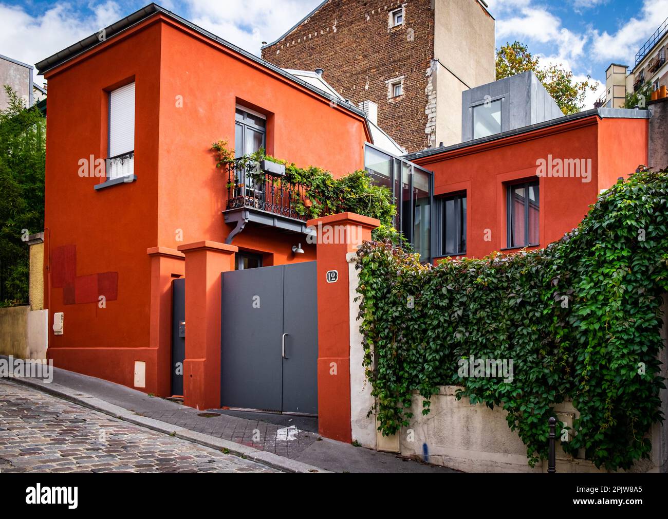 Paris, Frankreich, Okt. 2022, Blick auf ein modernes orangefarbenes Haus mit einer Wandabdeckung durch eine Kletterpflanze im Stadtteil Ménilmontant Stockfoto