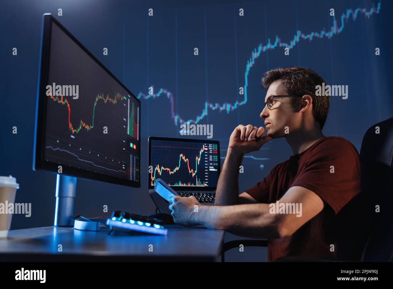 Seitenansicht eines konzentrierten Krypto-Händlers, der vor Computern sitzt, professionelle Analyse von Kerzenständerdiagrammen macht, Strategie erstellt, Stift und Notizblock hält, auf den Monitor schaut, das Kinn berührt Stockfoto