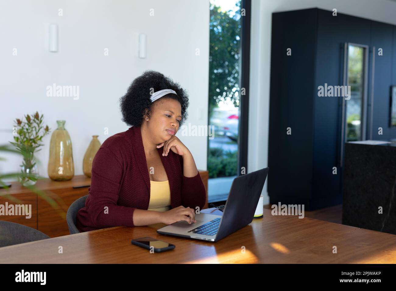 Eine große afroamerikanische Frau, die am Tisch sitzt und einen Laptop benutzt Stockfoto