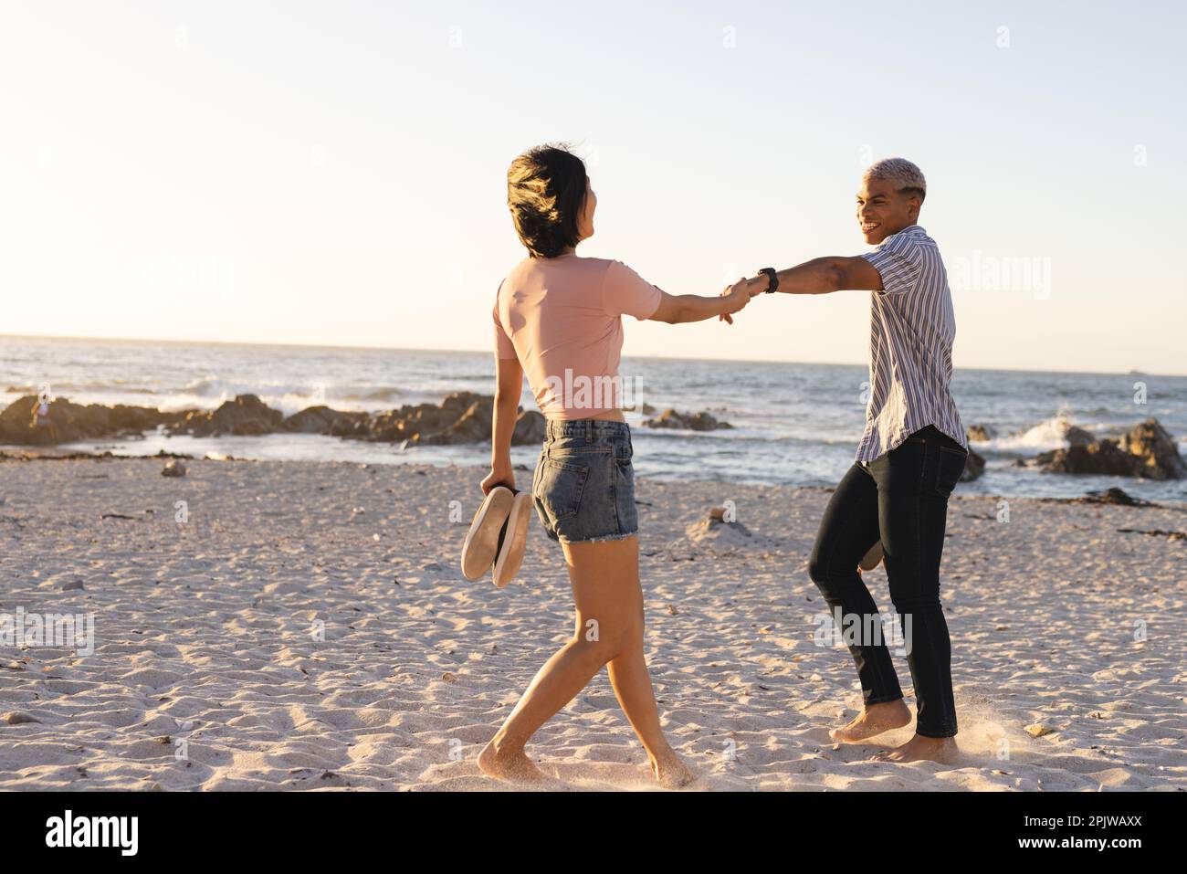 Glückliches, vielfältiges Paar, das Händchen hielt und am Strand spazierte Stockfoto