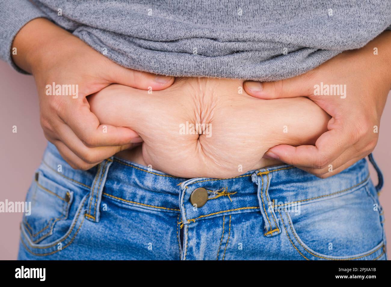 Eine dicke Frau mit übermäßigem Bauchfett auf rosa Hintergrund. Der übergewichtige Fettbauch der Frau. Weibliche Ernährung und Körpergesundheitskonzept Stockfoto