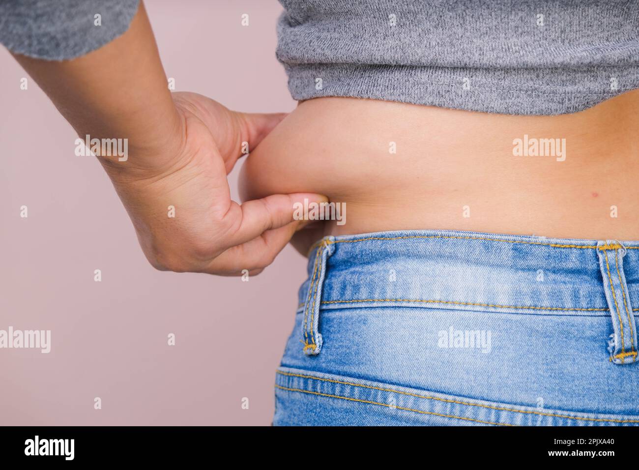 Eine dicke Frau mit übermäßigem Bauchfett auf rosa Hintergrund. Der übergewichtige Fettbauch der Frau. Weibliche Ernährung und Körpergesundheitskonzept Stockfoto