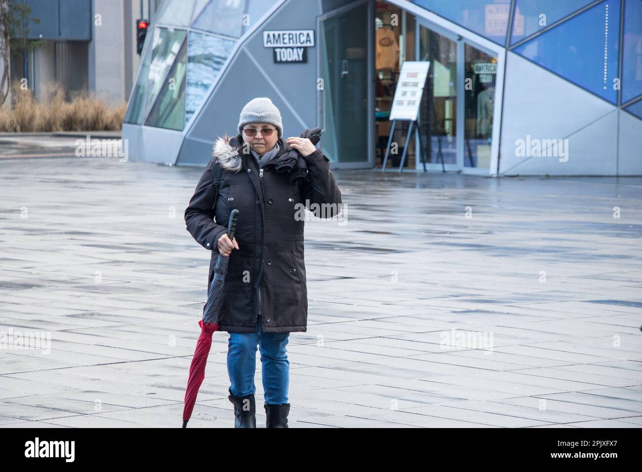 Eine Frau ein Regenmantel, der die Kapuze hochzieht, um sich vor dem Regen vor dem Hauptbahnhof Eindhoven zu schützen Stockfoto