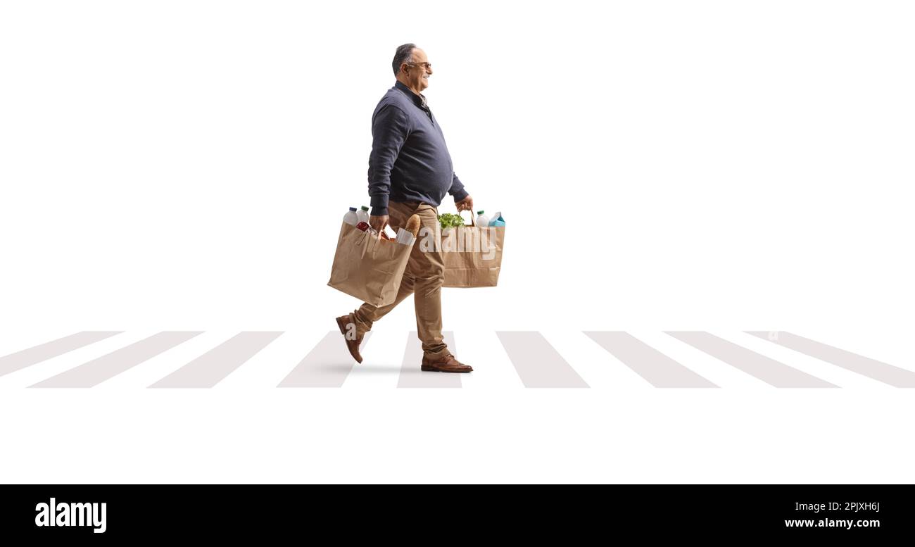 Profilaufnahme über die gesamte Länge eines erwachsenen Mannes, der Einkaufstüten trägt und das Fußgängerzebra überquert, isoliert auf weißem Hintergrund Stockfoto