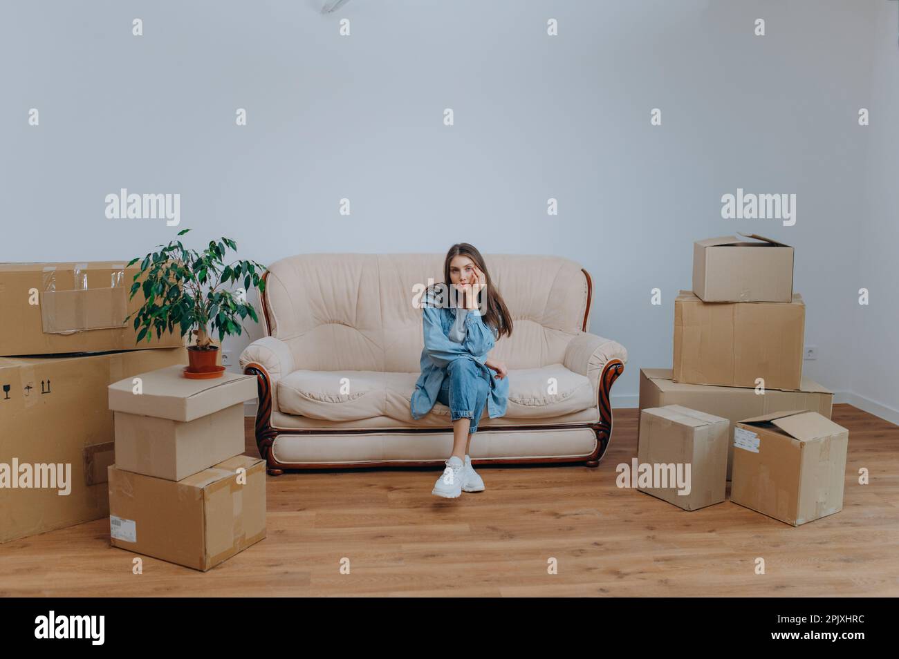 Eine Frau packt, um in eine neue Wohnung zu ziehen. Eine Frau sitzt auf einem Sofa neben Kartons Stockfoto