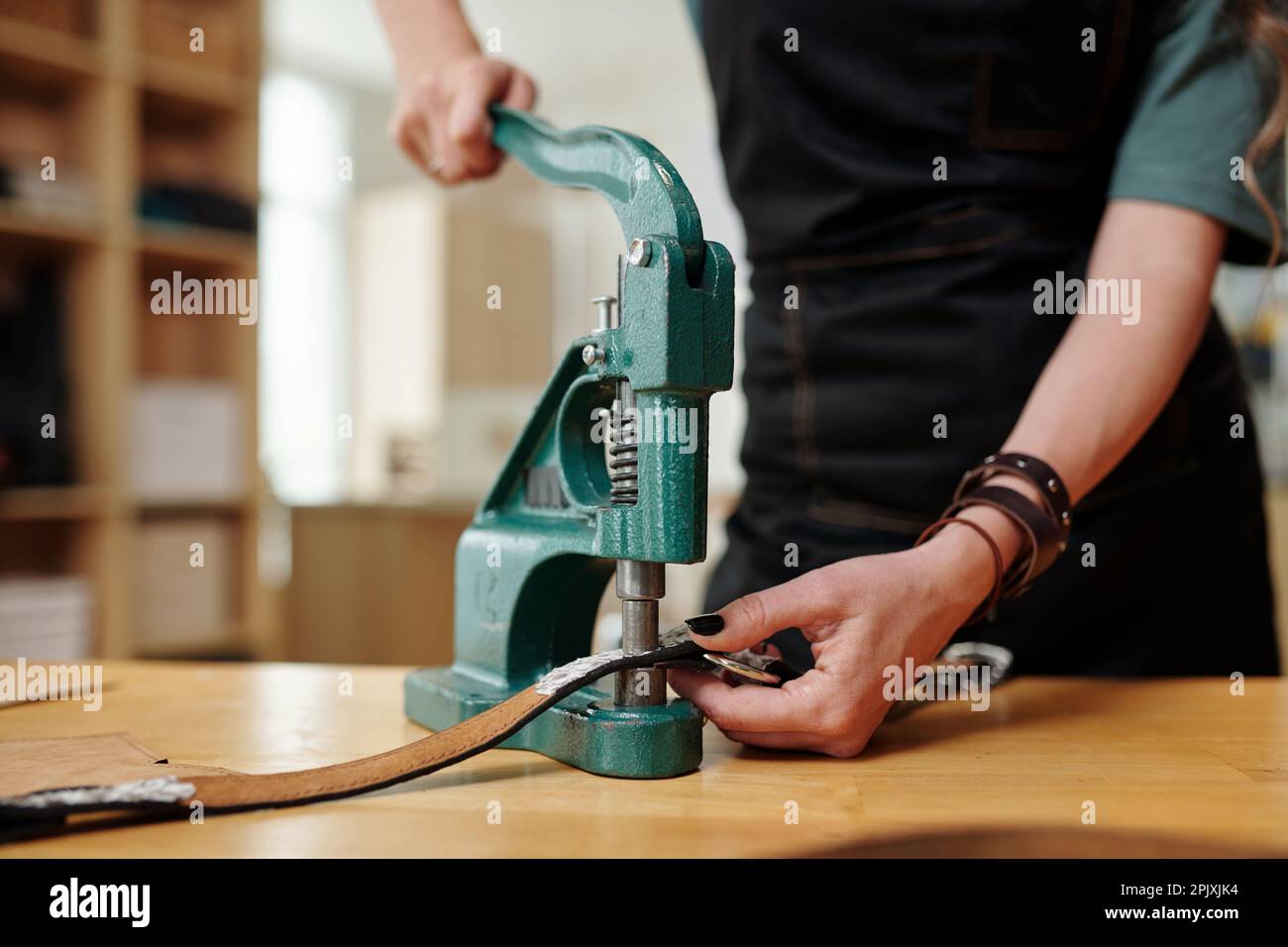 Handwerker mit Handpresse und Nieten beim Erstellen eines Ledergürtels für den Kunden Stockfoto