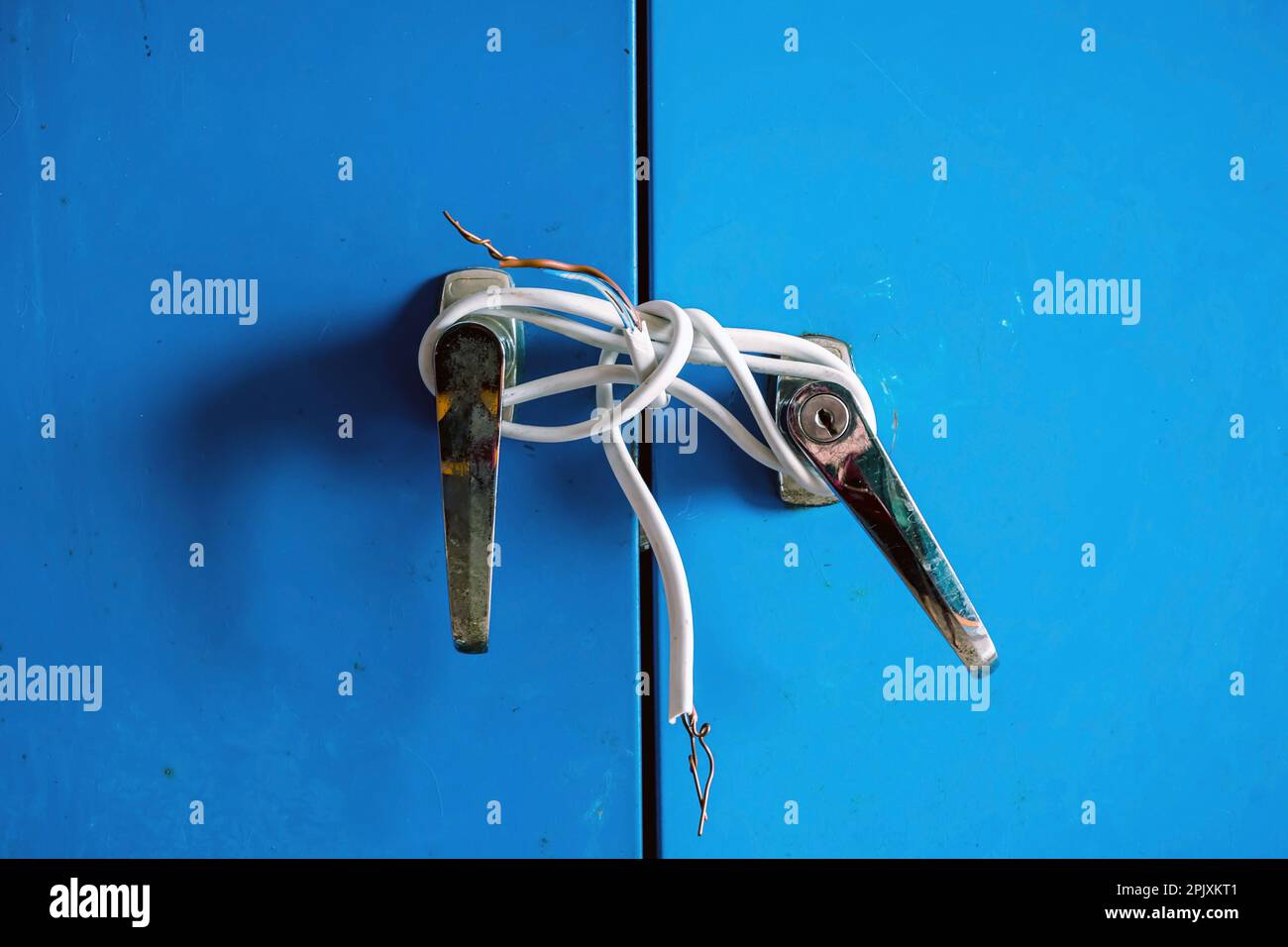 Bruchstücke weißer Elektrokabel wurden an silberne Knöpfe von Stahlschranktüren gebunden. Alte Tür mit Elektrokabel verriegelt. Blaues Schließfach mit o verriegelt Stockfoto
