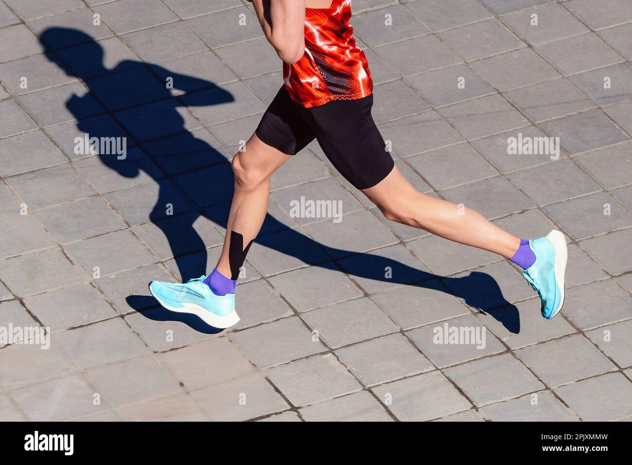 Top-View-Läufer-Athlet beim Marathonrennen, Schattenjogger auf Pflasterplatten, Kinesiotaping der Wadenmuskulatur Stockfoto