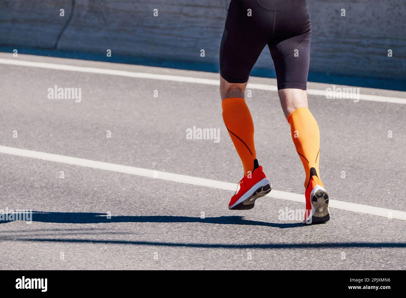 Beine männlicher Läufer in orangefarbenen Kompressionssocken und schwarzen Strumpfhosen laufen Rennen auf der Straße, Ausdauersport-Wettkampf Stockfoto