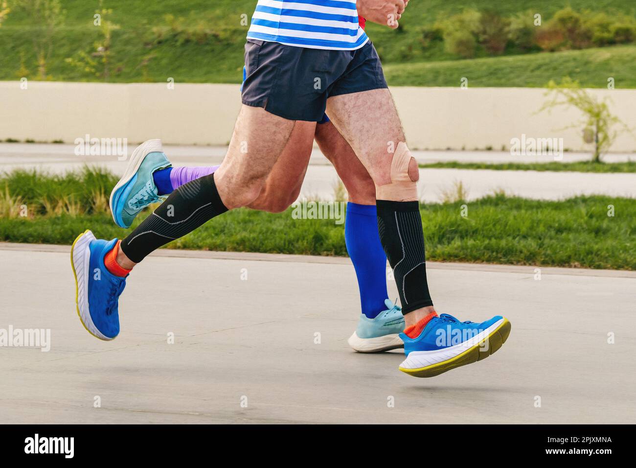 Beine zwei männliche Läufer in Kompressionssocken und Ärmeln laufen bei Marathonstrecken und Ausdauersportwettbewerben Stockfoto