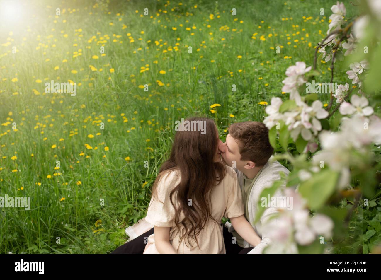 Eine schöne schwangere Frau geht in einem blühenden Garten spazieren. Ehemann, der schwangere Frau umarmt und küsst Stockfoto