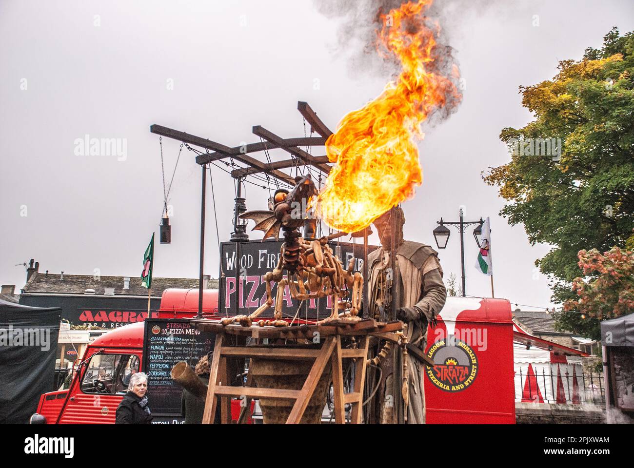 Beim Skipton International Puppet Festival zittern Flammen aus dem Mund eines feuerspeienden Drachen. Der Fahrer ist auf Pfählen, Stockfoto