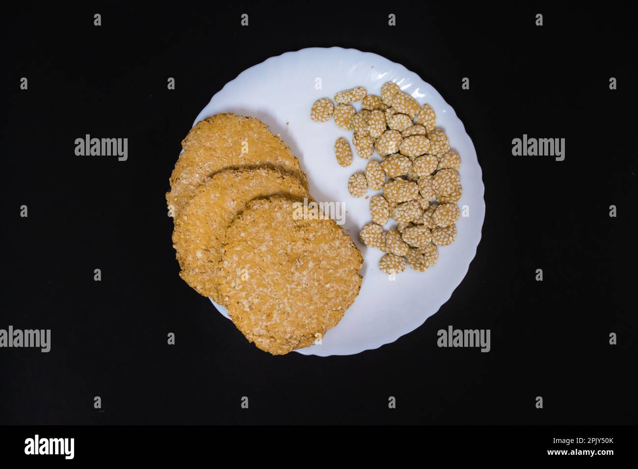 indische traditionelle süße Tilkut auf weißem Teller mit schwarzem Hintergrund Stockfoto