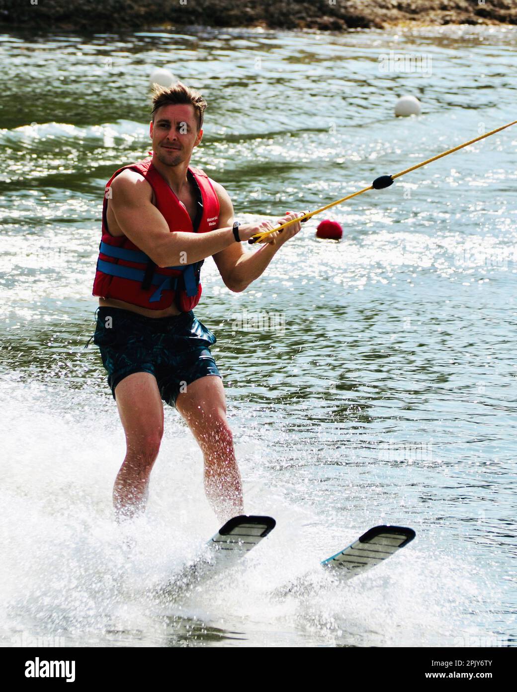 Ein erwachsener Mann, der Wasserskier trägt, hält eine Stange, während er im Wasser steht Stockfoto