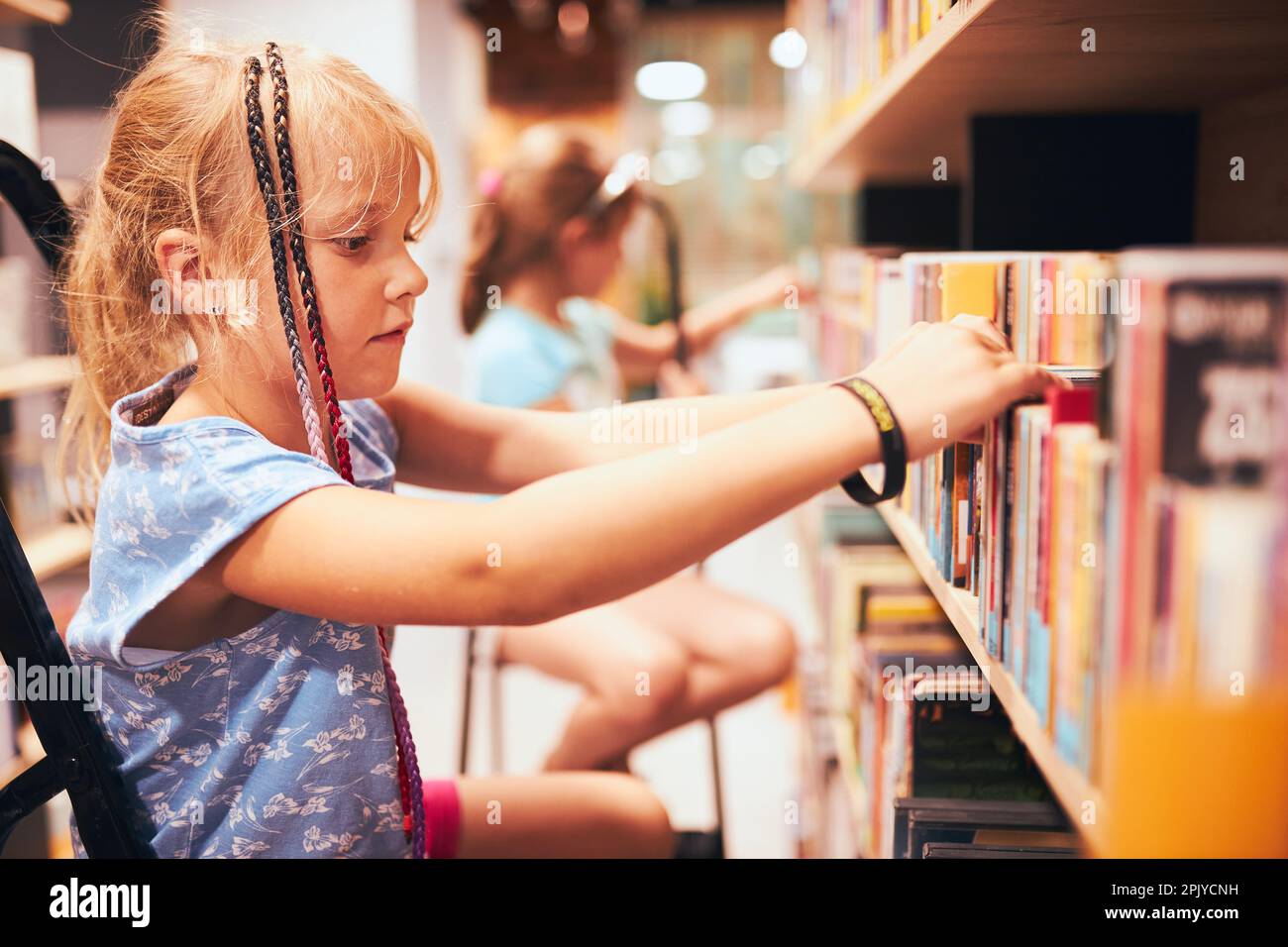 Schulmädchen, die Bücher in der Schulbibliothek suchen. Schüler wählen Bücher aus. Grundschule. Hausaufgaben machen. Aus Büchern lernen. Zurück in die Schule Stockfoto