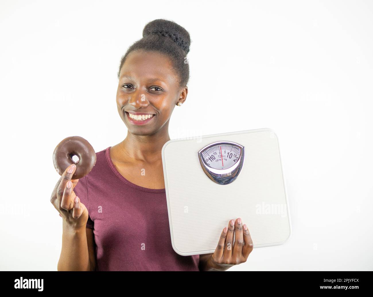 Junge Frau, die zwischen Gewichtsskala und Junk Food auf weißem Hintergrund wählt Stockfoto