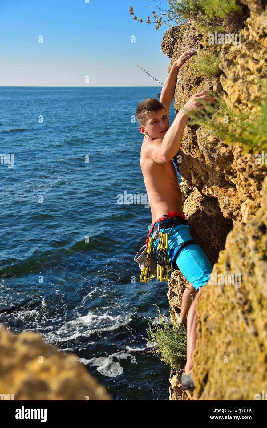 Junger Kletterer, der an einer Klippe auf einem Meereshintergrund hängt Stockfoto