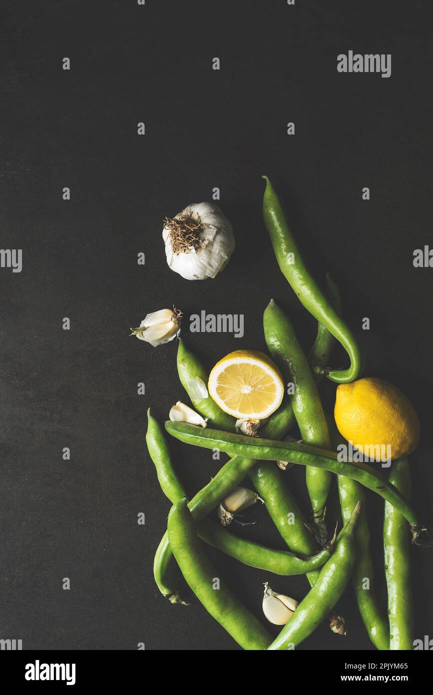 Frische grüne Faba-Bohnen mit Zitrone und Knoblauch auf schwarzem rustikalem Hintergrund, Tischaufnahme Stockfoto