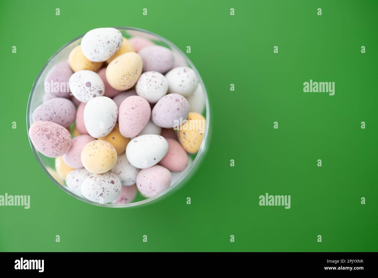 Rosafarbene, gelbe, weiße und violette Schokoladeneier in Glasschüssel auf grünem Hintergrund (Ostern) Stockfoto