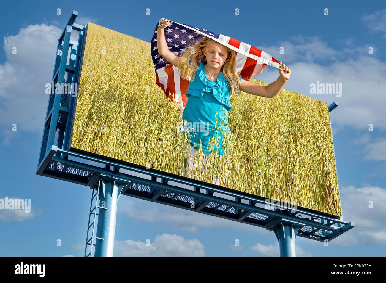 Reklametafelfoto eines jungen kaukasischen Mädchens, das mit einer amerikanischen Flagge in einem Weizenfeld mit Himmelshintergrund rennt Stockfoto