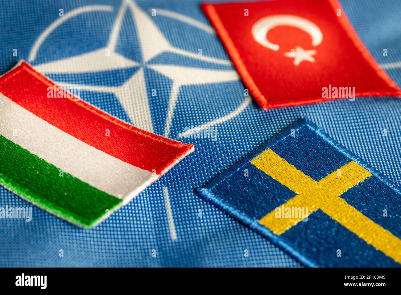 4. April 2023. Türkiye und Ungarn blockieren Schwedens Beitritt zur NATO. Flaggen Schwedens, Ungarns und der Türkei vor dem Hintergrund des Symbos der Verteidigungsallianz Stockfoto