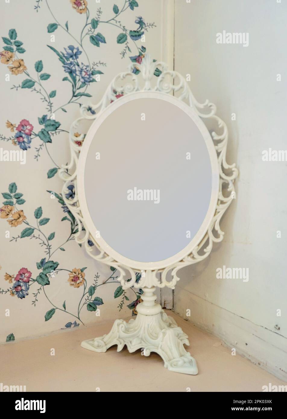 Altmodischer elfenbeinfarbener Spiegel auf einem Sockel mit Tapetenhintergrund im Retro-Blumendesign Stockfoto