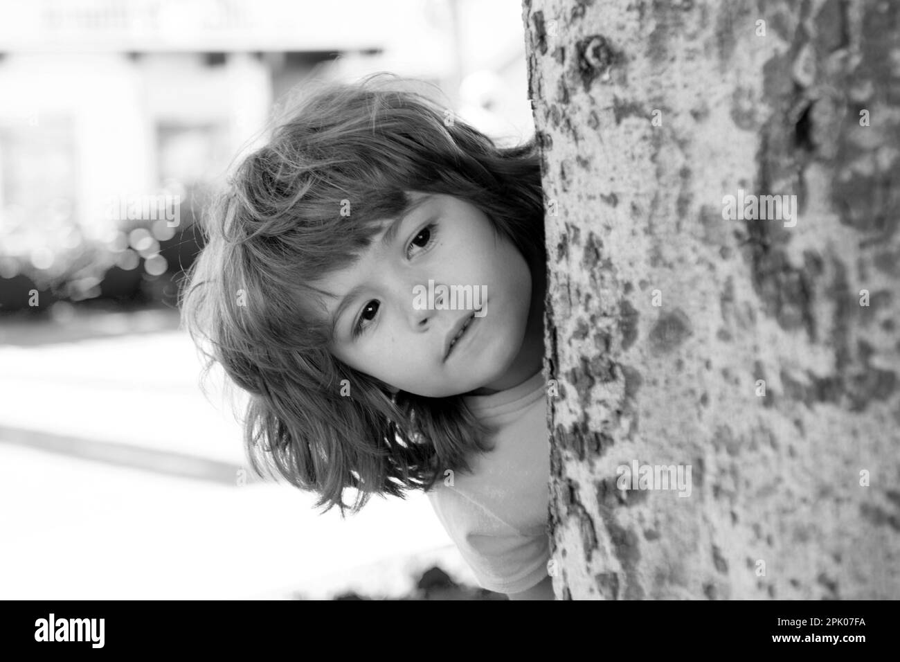 Verstecken und suchen. Peekaboo. Kleines Kind versteckt sich am Baum. Kinderurlaub. Stockfoto