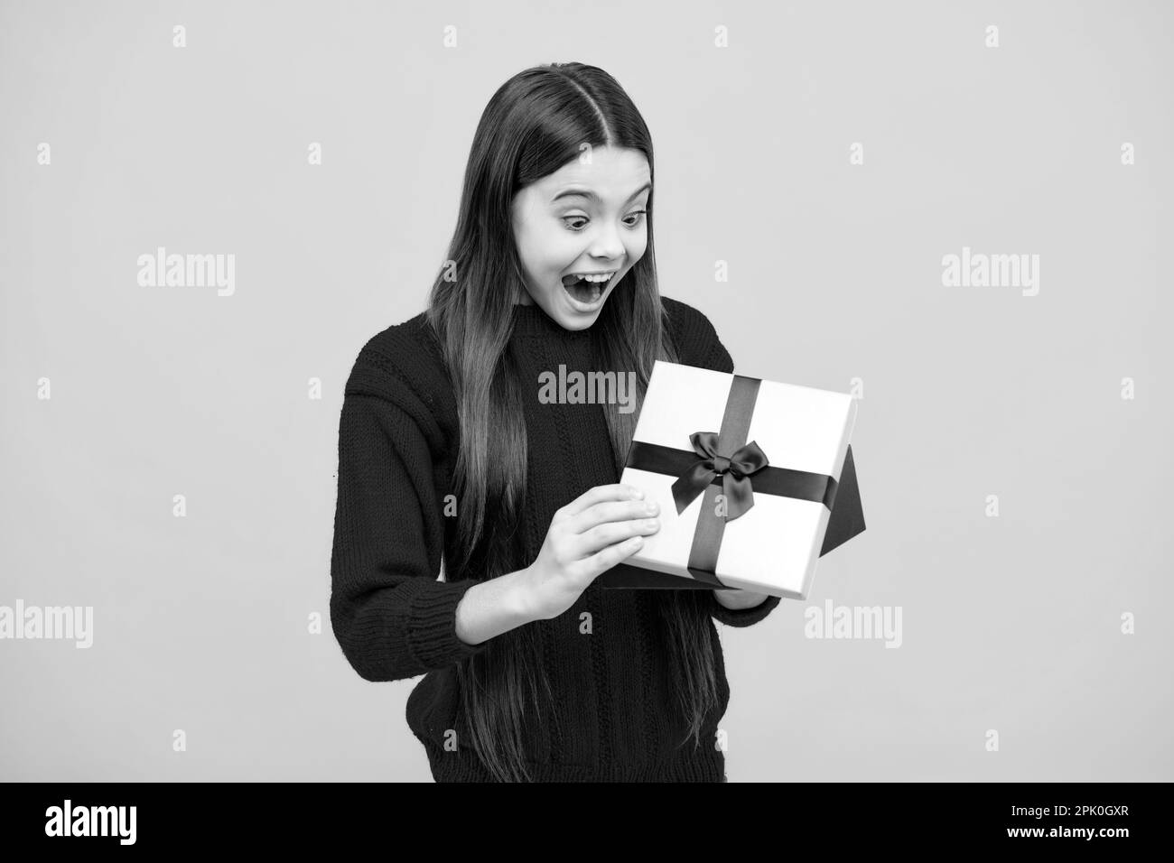 Überraschende Emotionen eines jungen Teenagers. Kind Teenager Mädchen 12-14 Jahre alt mit Geschenk auf isoliertem Hintergrund. Geburtstag, Feiertagskonzept. Teenager halten Stockfoto