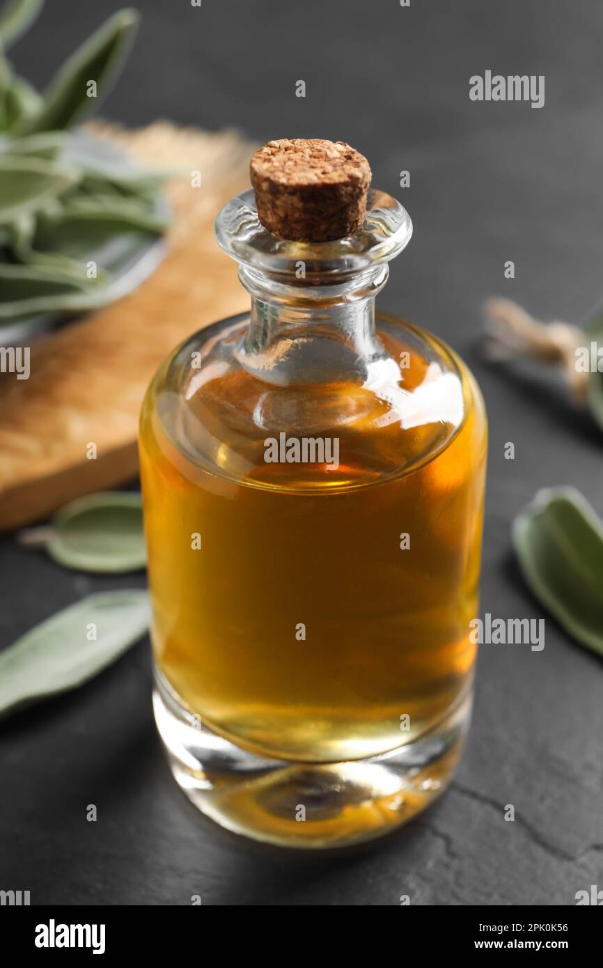Flasche ätherisches Salbeiöl und Blätter auf schwarzem Tisch Stockfoto