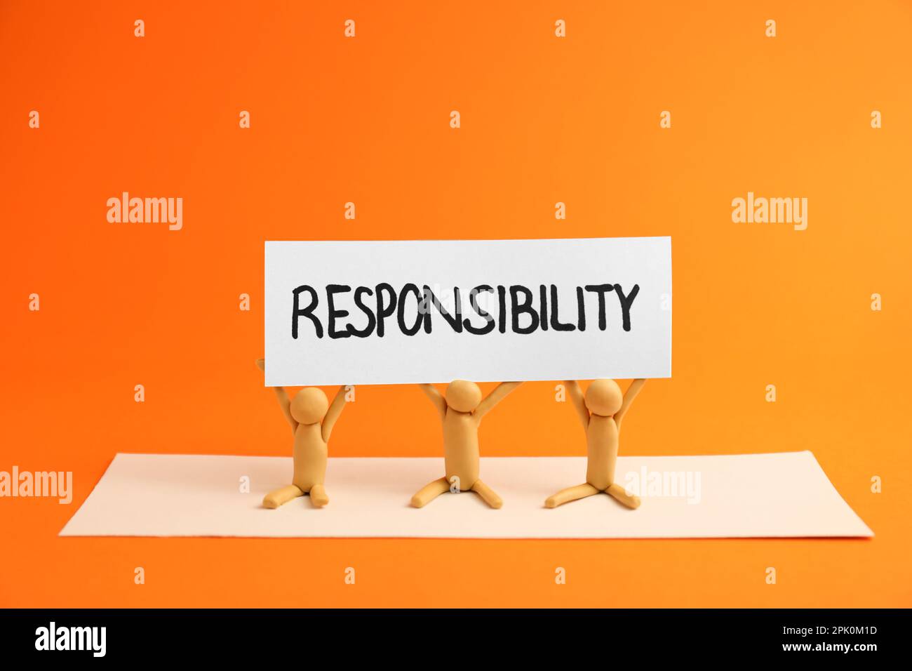 Drei plastische menschliche Figuren mit einer Karte mit dem Wort Verantwortung auf orangefarbenem Hintergrund Stockfoto
