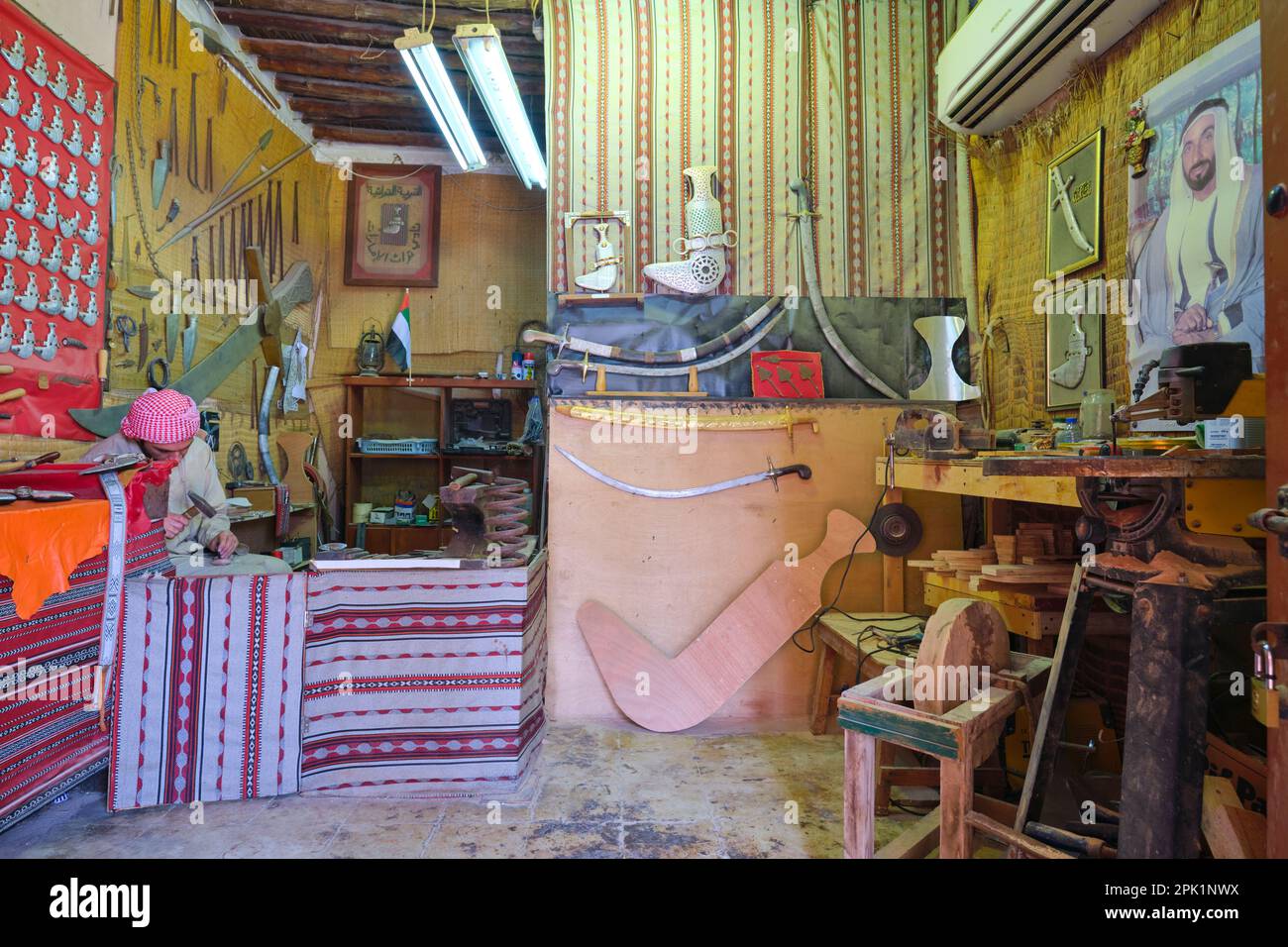 Ein lokaler Handwerker in seinem Laden, der Metallschwerter und Dolche herstellt. Im Emirates Heritage Club Heritage Village in Abu Dhabi, Vereinigte Arabische Emirate. Stockfoto