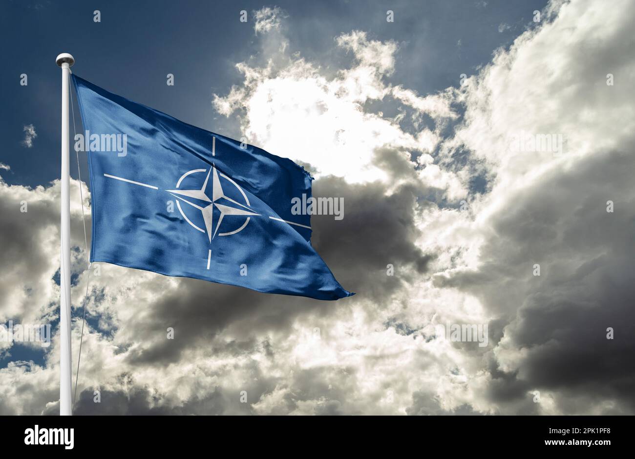 Die Flagge der NATO winkt im Wind auf einem Fahnenmast gegen den Himmel Stockfoto