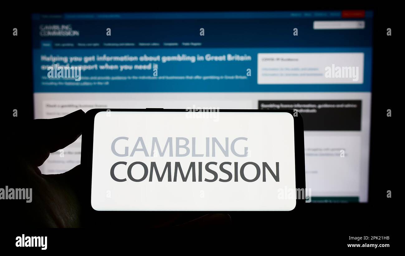 Person, die ein Mobiltelefon mit dem Logo der britischen öffentlichen Körperschaft Gambling Commission auf dem Bildschirm vor der Webseite hält. Konzentrieren Sie sich auf das Display des Telefons. Stockfoto